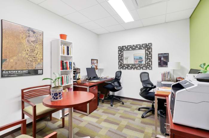 Shared office with two desks, artwork, and a loaded bookshelf in Central Park location