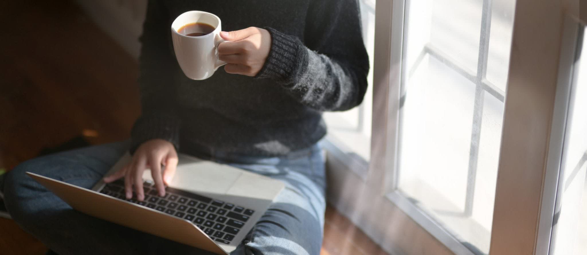 A person working from their laptop as drinking coffee at home during the coronavirus.